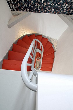 Transformation spectaculaire d’une cage d’escalier d’une ancienne bâtisse.  Peinture rouge orangé de l’escalier et papier-peint aux motifs océaniques contrastent à merveille avec le gris pâle des boiseries