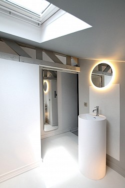 Salle de bain épurée dans un espace très exigu. Blancheur et jeu de miroirs pour capter la lumière naturelle de la fenêtre de toit
